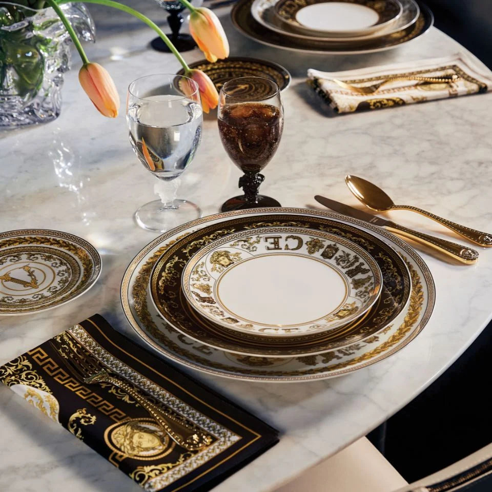 Elegant table setting with gold and black decorative plates, glasses, and cutlery on a marble surface.